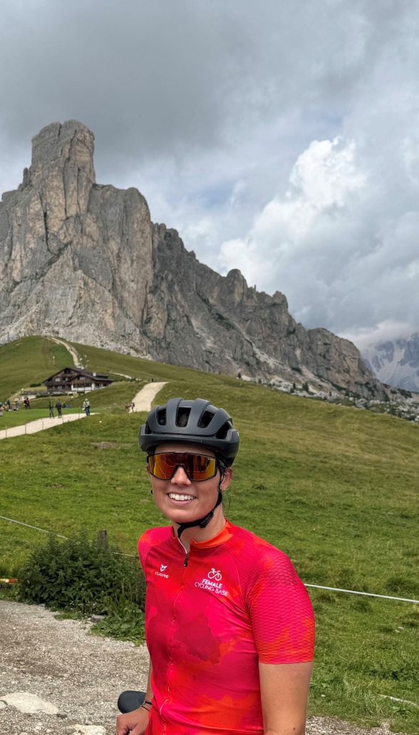 Radfahrerin in rotem Trikot, sowie Helm und Brille macht in einem Gebirge ein Foto