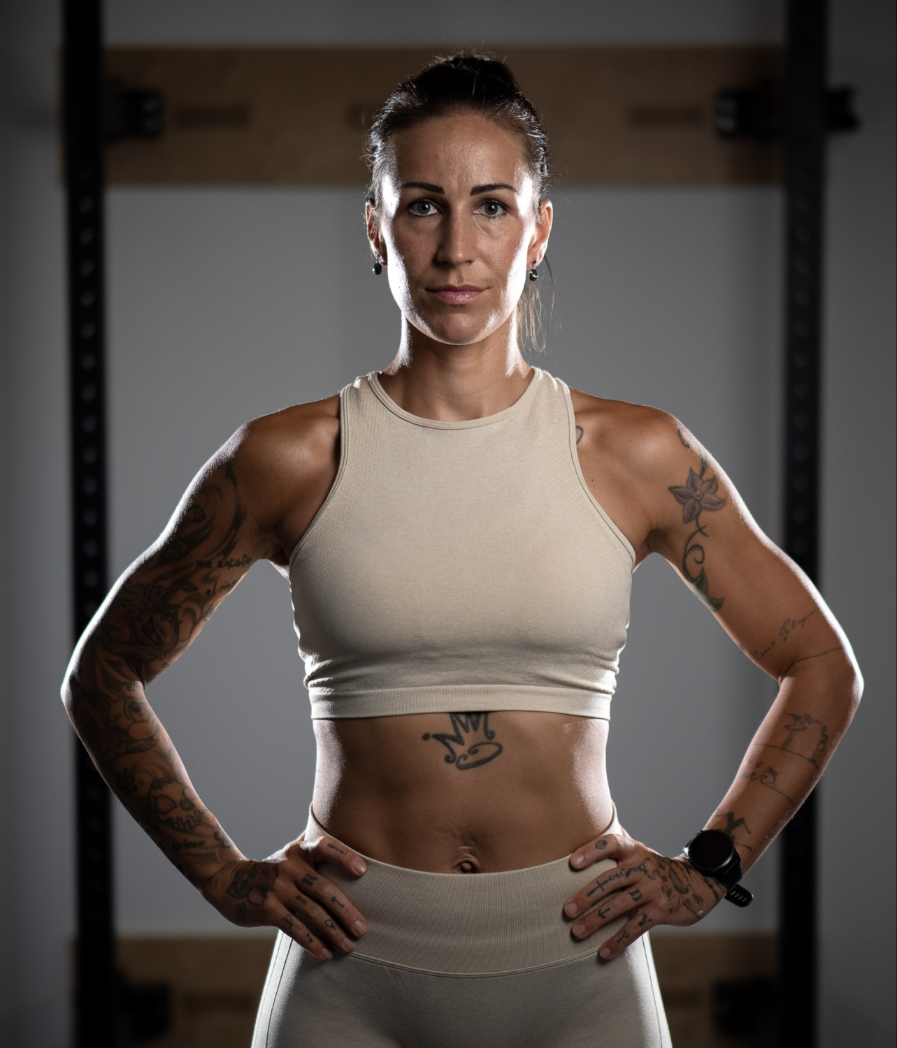 Frau in mittlerem Alter mit Tattoos, kleinen Ohringen, Sportuhr und in Sportkleidung gekleidet.
