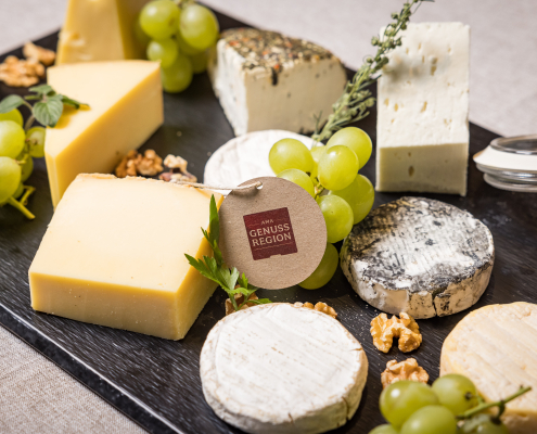 Vielfältige Käseplatte mit Hart- und Weichkäse, dekoriert mit grünen Trauben, Walnüssen und einem Anhänger "AMA Genuss Region".