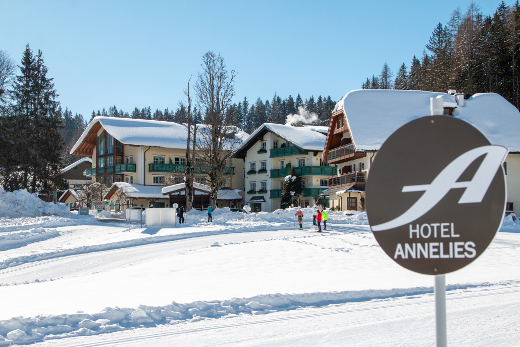 Hotel Annelies - Außenansicht - Winter Im Vordergrund das Schild"Hotel Annelies". Dahinter das schneebedeckte Hotel. Davor eine schneebedeckte Anlage für Langläufer.