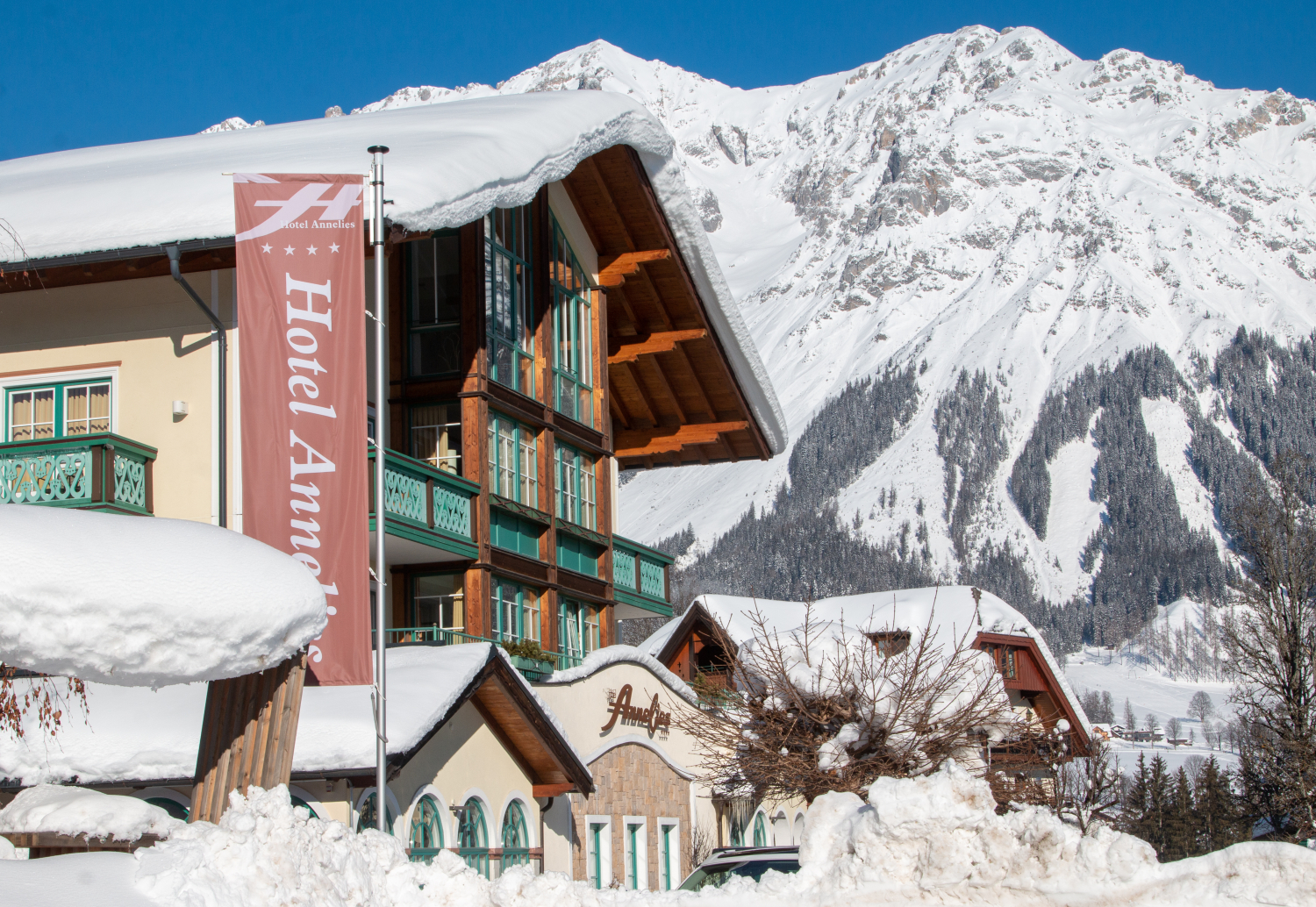 Verschneites Hotel in den Alpen mit großem Schild „Hotel Annelies“ vor beeindruckender Bergkulisse.