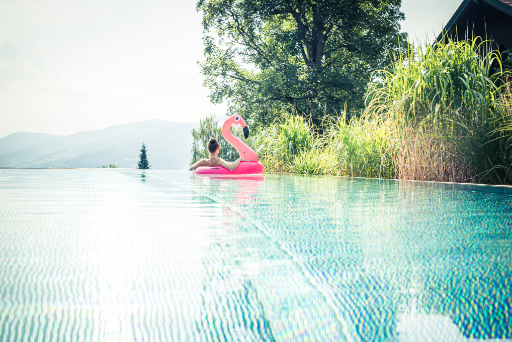 Infinity Pool des Hotel Annelies Eine Frau entspannt sich auf einem Flamingo-Schwimmreifen im Infinity Pool. Im Hintergrund sind Bäume und Gräser, sowie eine Bergfront zu sehen.