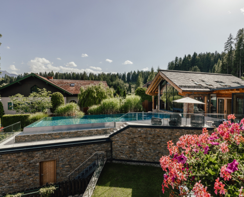 Modernes Anwesen inmitten grüner Natur mit stilvollem Infinity-Pool, gemütlicher Terrasse und blühendem Garten, umgeben von Bäumen.