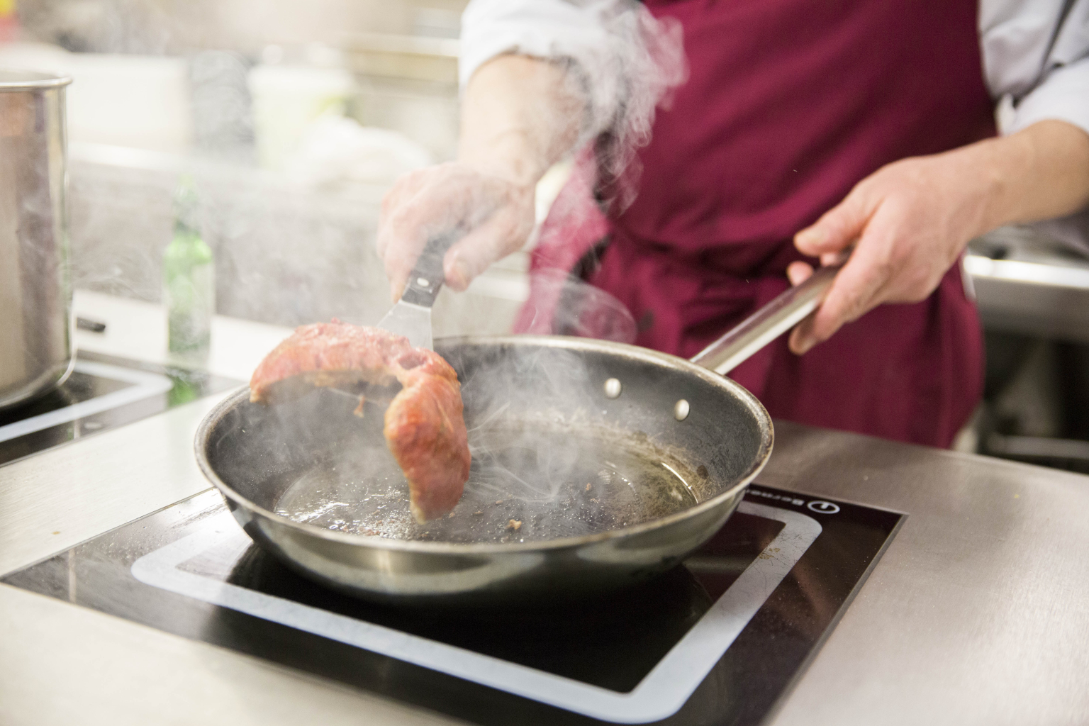 Ein Koch wendet ein Stück Fleisch in einer Pfanne.