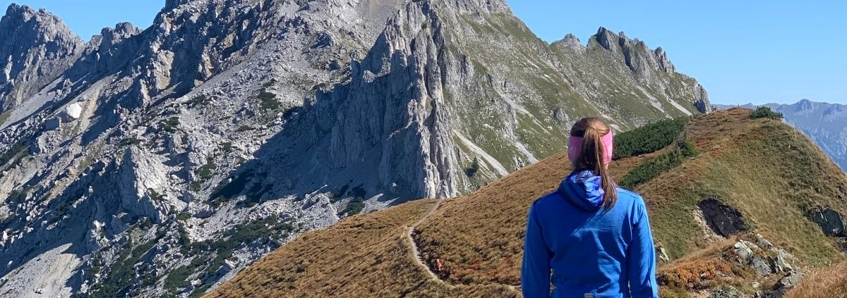 Bild einer Dame in Sportkleidung von hinten, wie sie einen Bergpfad entlang geht.