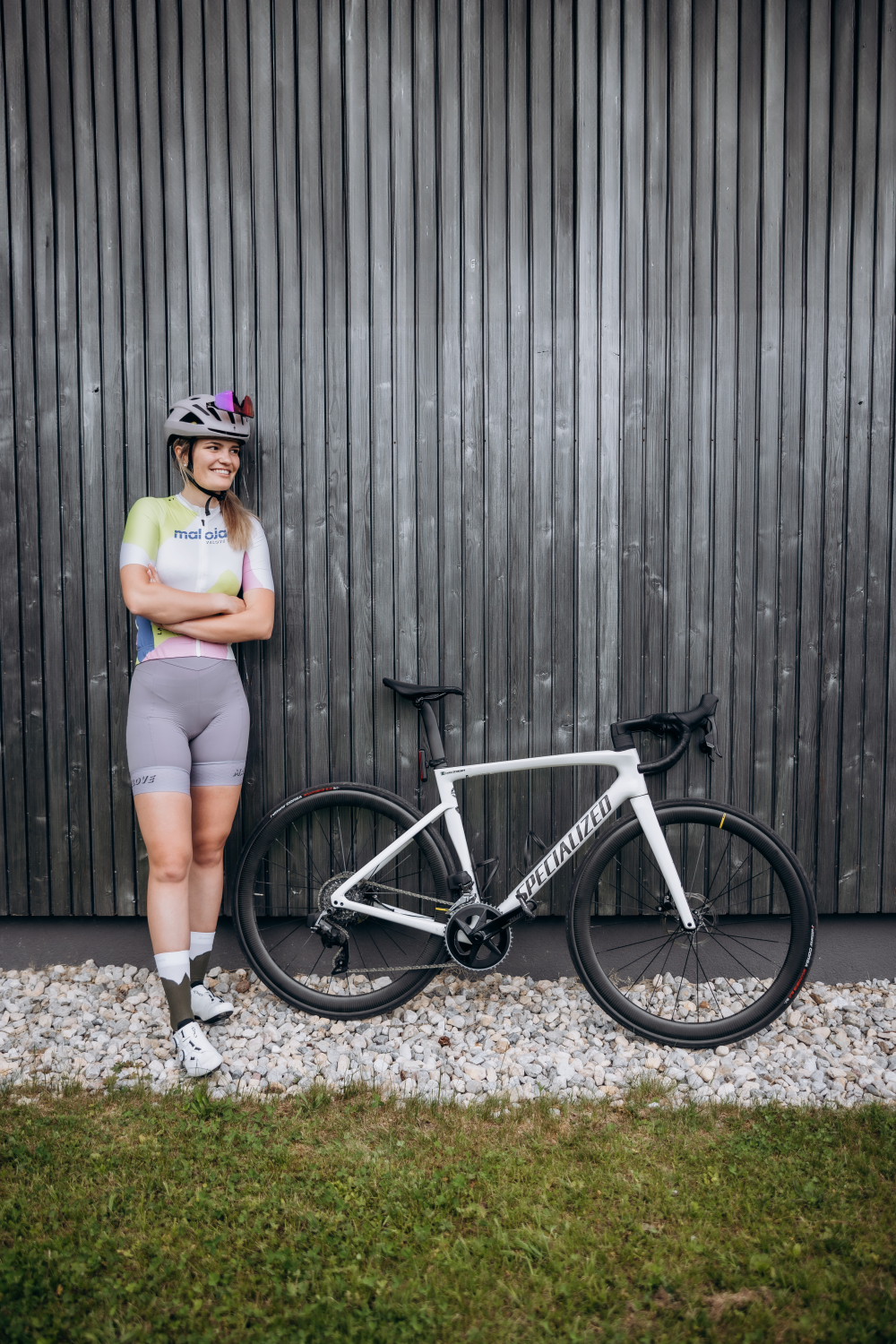 Lächelnde Radfahrerin mit Helm und Fahrrad, lehnend an einer Holzwand