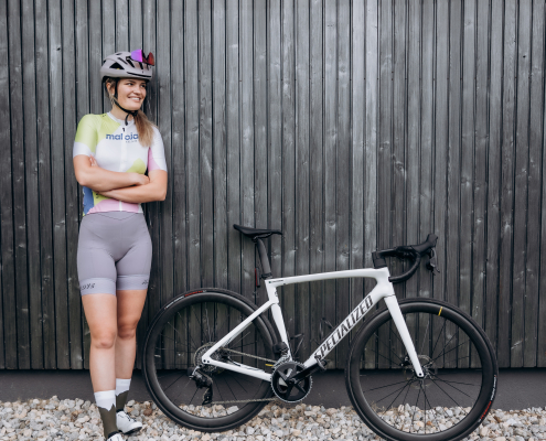 Lächelnde Radfahrerin mit Helm und Fahrrad, lehnend an einer Holzwand